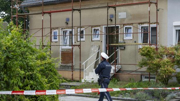 Ein Polizist steht vor einem mit Absperrband gesicherten Haus, das von Baugerüsten umgeben ist.