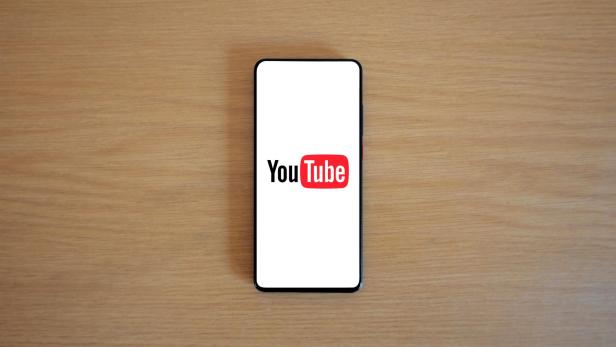 Smartphone mit YouTube-Logo auf dem Bildschirm liegt auf einem Holztisch.