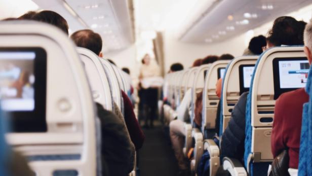 Flugzeugkabine mit Passagieren in den Sitzreihen und einer Flugbegleiterin im Gang.