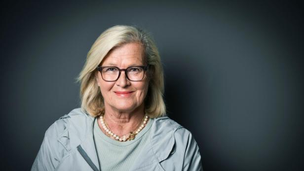 Ein Potraitfoto von Ursula Plassnik, fotografiert vor dunklem Hintergrund, sie schaut freundlich direkt in die Kamera