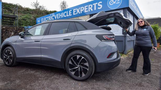 Frau öffnet Kofferraum eines Elektroautos bei einem Gebrauchtwagenhändler.