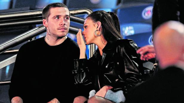 Brooklyn Beckham und Nicola Peltz sitzen nebeneinander auf der Tribüne eines Stadions und unterhalten sich.