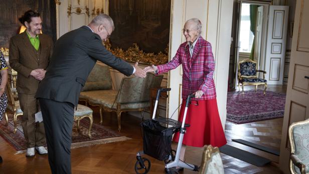 Königin Margrethe II. von Dänemark begrüßt einen Mann mit Handschlag, während sie sich auf einen Rollator stützt.