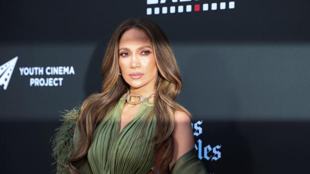 Jennifer Lopez posiert in einem olivgrünen Kleid vor einer Wand mit dem Logo des Youth Cinema Project.