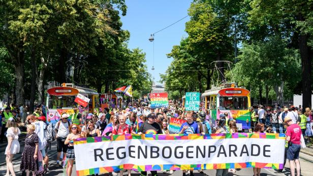 Viele Protestierende auf die Vienna ride Regenbogenparade halten einen großen banner. Im Hintergrund sind bunte Fahnen.