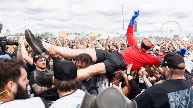 Eine verkleidete Person wird beim Crowdsurfing von einer großen, feiernden Menschenmenge getragen.