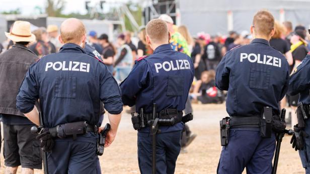Mehrere Polizisten stehen mit dem Rücken zur Kamera vor einer Menschenmenge bei einer Veranstaltung.