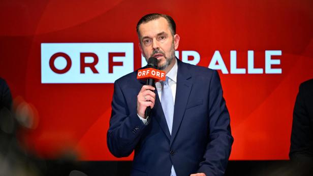 Ein Mann im Anzug spricht vor einem roten Hintergrund mit dem Schriftzug „ORF für alle“ in ein Mikrofon mit ORF-Logo.