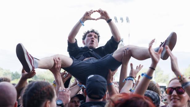 Eine Menschenmenge trägt eine Person beim Crowdsurfing, die mit den Händen ein Herz formt.