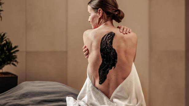 Eine Frau mit hochgesteckten Haaren sitzt mit einem weißen Handtuch und schwarzer Maske auf dem Rücken.