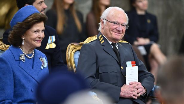 König Carl XVI. Gustaf und Königin Silvia von Schweden sitzen bei einer offiziellen Veranstaltung in festlicher Kleidung nebeneinander.