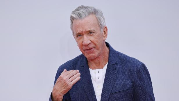 Schauspieler Tim Allen trägt ein weißes Hemd unter einem dunkelblauen Sakko vor einem hellen Hintergrund.
