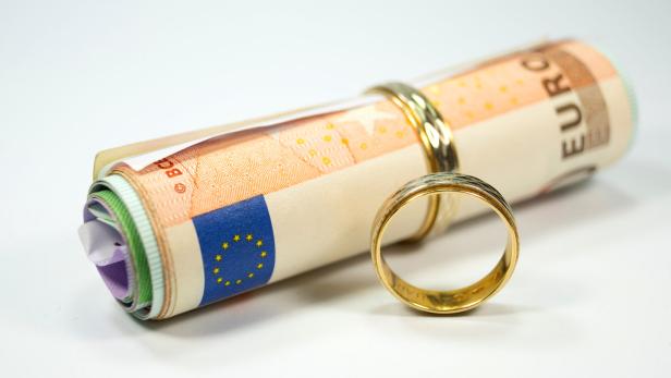 Zusammengerollte Eurobanknoten mit zwei goldenen Ringen auf weißem Hintergrund.