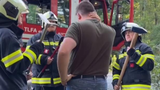 Drei Feuerwehrleute in Uniform sprechen mit einem Mann vor einem Einsatzfahrzeug im Grünen.