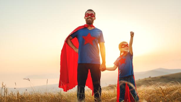 concept of father's day. dad and child daughter in hero superhero costume at sunset