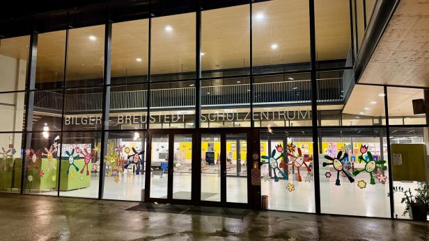 Großes, beleuchtetes Schulgebäude mit Glasfassade, bunten Kinderzeichnungen und dem Schriftzug „Bilger Breustedt Schulzentrum“.