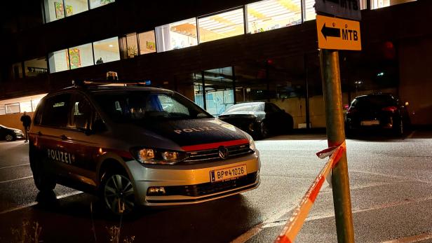 Ein österreichischer Polizeiwagen steht nachts vor einem beleuchteten Gebäude, abgesperrt durch ein rot-weißes Absperrband.