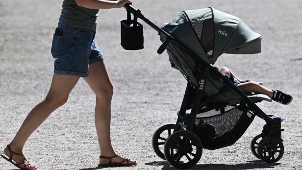 Eine Person schiebt einen Kinderwagen mit einem sitzenden Kind auf einem sonnigen Weg.