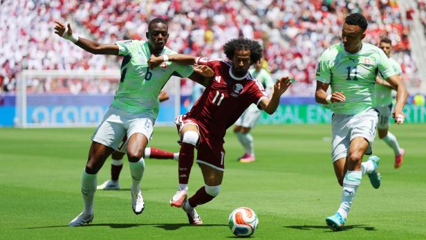 Zwei Spieler der Schweiz in hellgrünen Trikots kämpfen gegen einen katarischen Spieler in einem dunkelroten Trikot um den Ball.