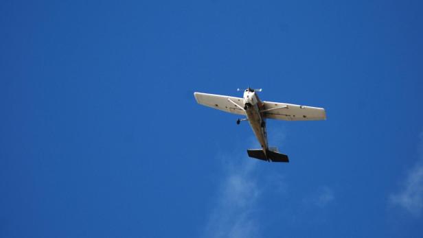 Kleinflugzeug fliegt vor blauem Himmel, von unten aufgenommen.