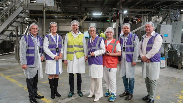 Sieben Personen mit Schutzanzügen stehen in einer Produktionshalle