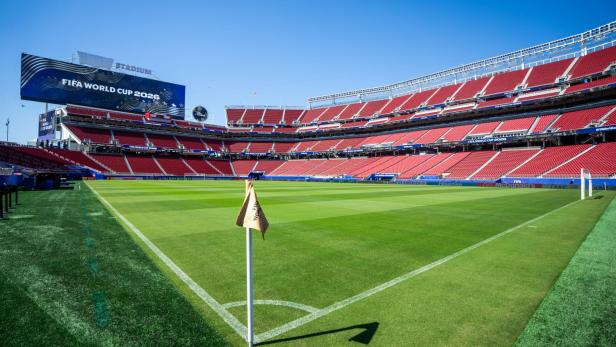 Ein leeres Fußballstadion mit roten Sitzen und einer großen Anzeigetafel für die FIFA World Cup 2026 unter blauem Himmel.