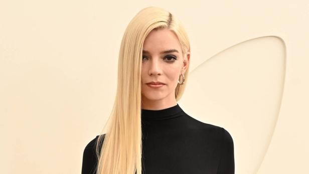Anya Taylor-Joy mit langem, blondem Haar und schwarzem Oberteil vor einem hellen Hintergrund.
