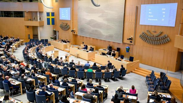 Schwedischer Reichstag mit vielen Abgeordneten bei einer Abstimmung, Ergebnis auf den Bildschirmen sichtbar.
