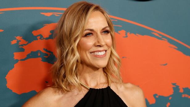 Sheryl Crow lächelt vor einem Hintergrund mit einer stilisierten Weltkarte.