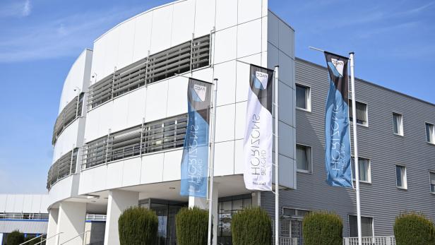 Das moderne Firmengebäude von FACC mit blauen und weißen Werbefahnen vor einer hellen Fassade unter blauem Himmel.