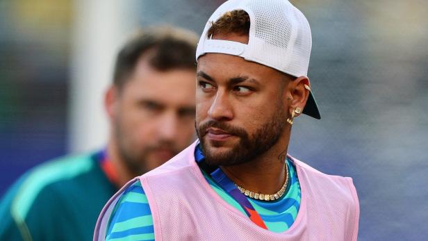 Neymar trägt eine weiße Kappe und ein pinkes Überziehshirt vor einem unscharfen Hintergrund.