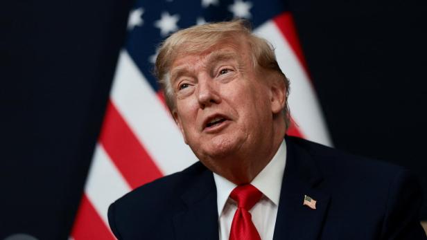Donald Trump im Anzug mit roter Krawatte vor einer US-Flagge.
