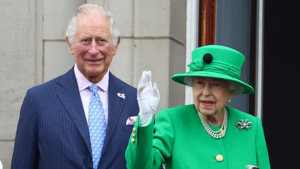 Charles steht neben Queen Elizabeth II., die in einem grünen Kostüm winkt.