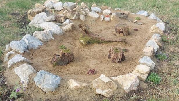 Kleines rundes Steingartenbeet mit Sandfläche und Baumstümpfen im Park.