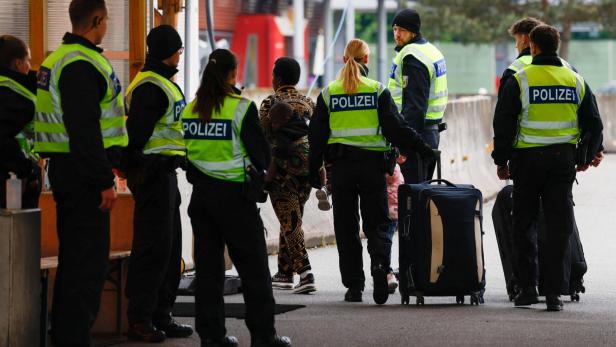 Mehrere Polizisten in Warnwesten begleiten Reisende mit Koffern auf einem Bahnhofsgelände.
