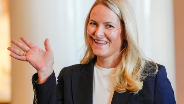 Kronprinzessin Mette-Marit von Norwegen lächelt freundlich und winkt mit der Hand, während sie eine Nasenbrille zur Sauerstoffzufuhr trägt.