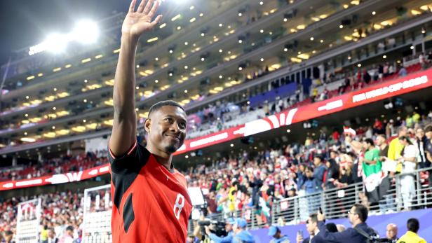 David Alaba winkt in einem roten Trikot vor jubelnden Zuschauern in einem beleuchteten Stadion.