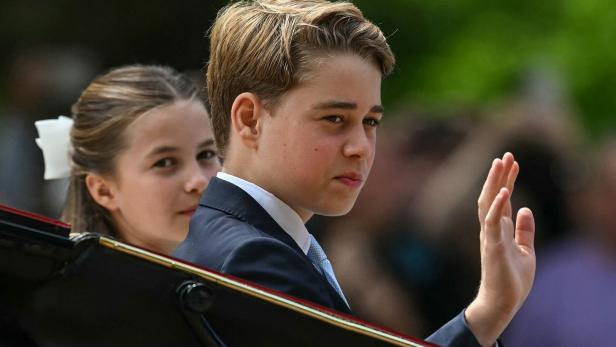 Prinz George winkt aus einer Kutsche, während Prinzessin Charlotte hinter ihm sitzt.