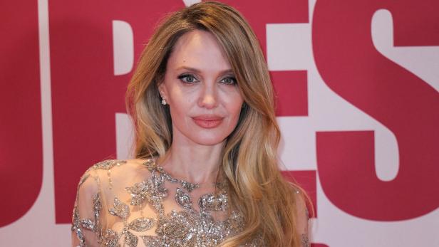 Angelina Jolie trägt ein mit Pailletten verziertes Kleid vor einem roten Hintergrund.