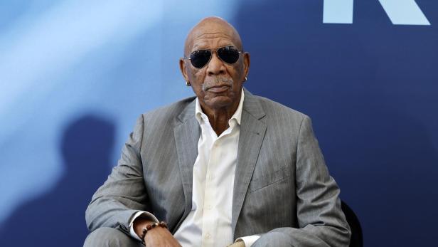 Morgan Freeman trägt einen grauen Anzug, ein weißes Hemd und eine Sonnenbrille vor einem dunkelblauen Hintergrund.