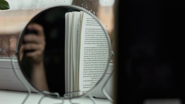 Vergrößerungsspiegel am Fenster reflektiert Sonnenlicht auf ein Buch.