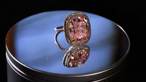 Ein Ring mit einem großen, pinkfarbenen Diamanten liegt auf einer spiegelnden Oberfläche.