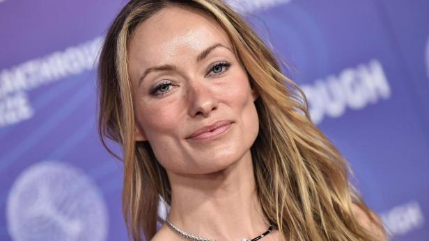 Olivia Wilde lächelt vor einem violetten Hintergrund in die Kamera.