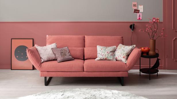 Pinkes Sofa in einem kleinen, stilvoll eingerichteten Wohnzimmer mit Kissen, Wanddeko und Beistelltisch.
