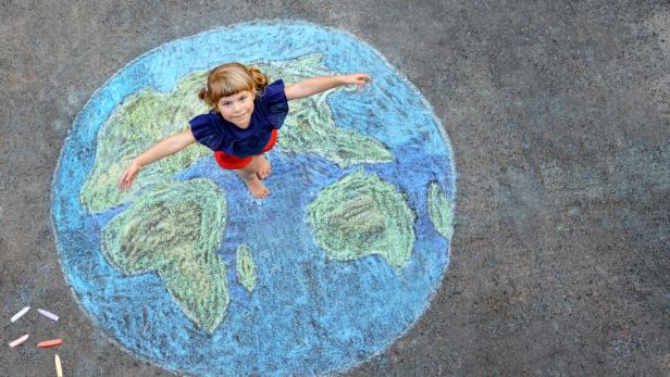 Little preschool girl with earth globe painting with colorful chalks on ground. Positive toddler child. Happy earth day concept. Creation of children for saving world, environment and ecology.