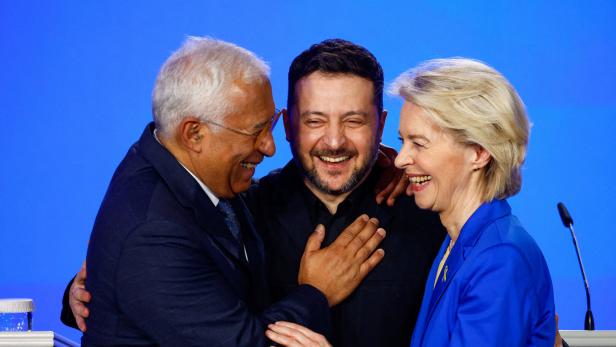 António Costa, Wolodimir Selenskij und Ursula von der Leyen lachen gemeinsam vor einem blauen Hintergrund.