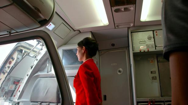Eine Flugbegleiterin in roter Uniform steht in der geöffneten Flugzeugkabine und blickt zur Tür hinaus.