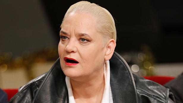 Hella von Sinnen blickt in schwarzer Lederjacke und weißer Bluse zur Seite.