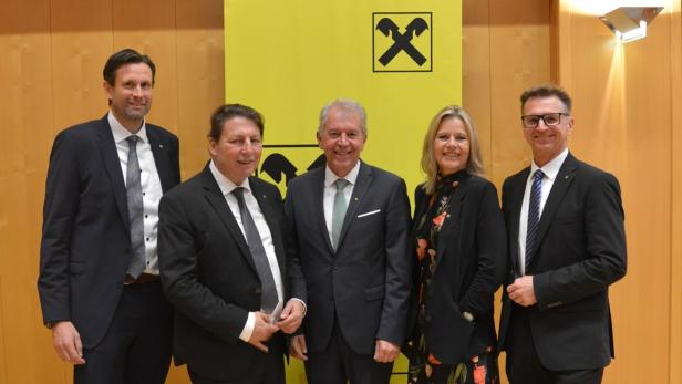 Fünf Personen in Anzügen stehen vor einem gelben Hintergrund mit schwarzem Bergbau-Logo und lächeln in die Kamera.