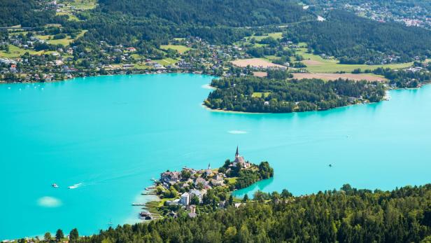 Blick auf den türkisblauen Wörthersee mit einer kleinen Halbinsel und Kirche.